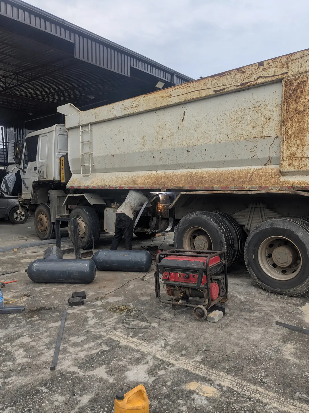 Technicians completing dual-fuel conversion work on a heavy truck in a workshop yard